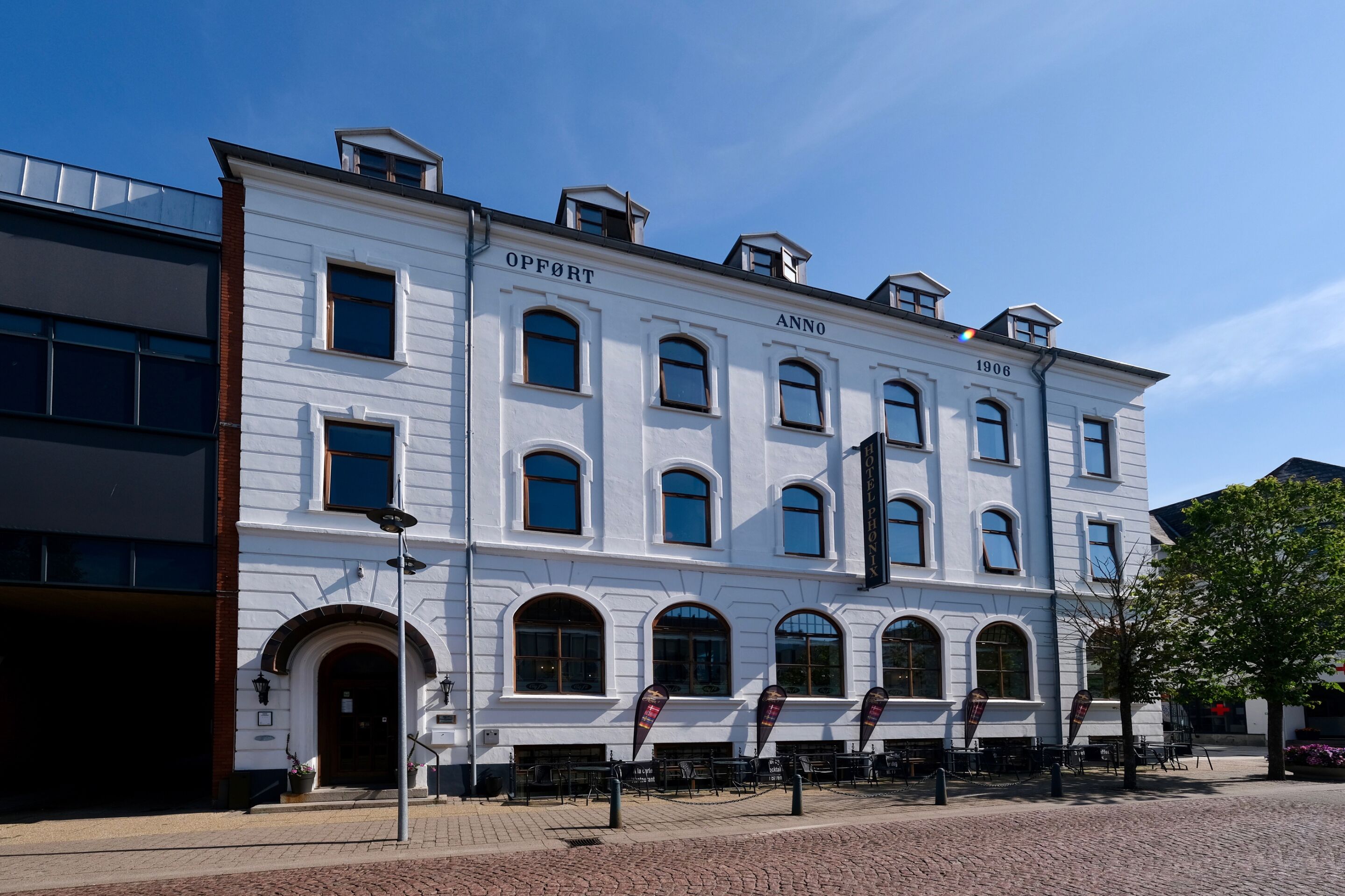 En hvid bygning med buede vinduer og et skilt, der siger "OFFORT ANNO 1906".