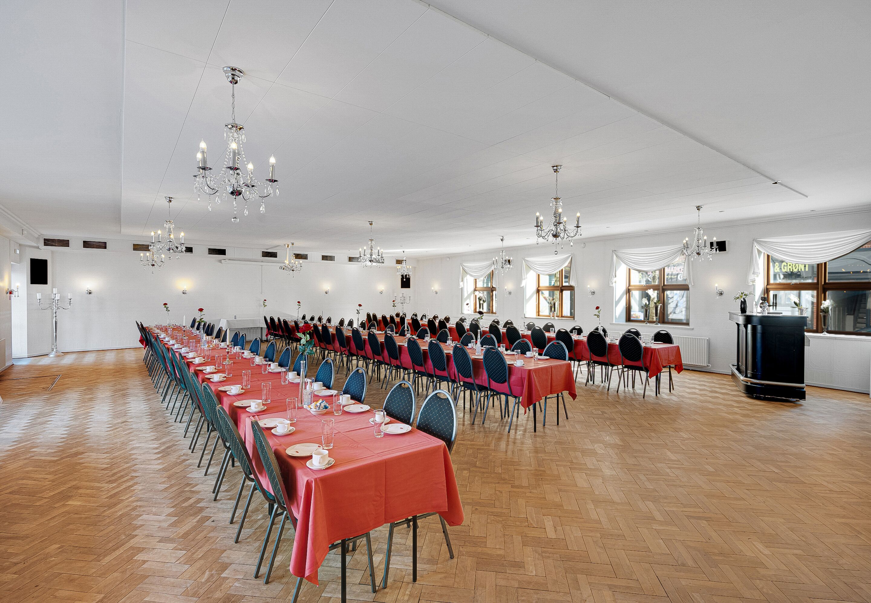 Une vaste salle de banquet avec de longues rangées de tables, des lustres et une cheminée.