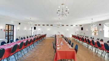 A large conference room with long tables, chairs, chandeliers, and a wooden floor.