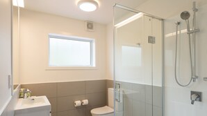 A modern bathroom with a glass-enclosed shower, a toilet, a sink, and a window. - Heartland Hotel Glacier Country (Fox Glacier)