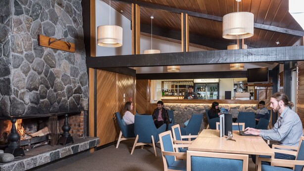 A modern interior with a stone fireplace, wooden ceiling beams, and a bar area. - Heartland Hotel Glacier Country (Fox Glacier)