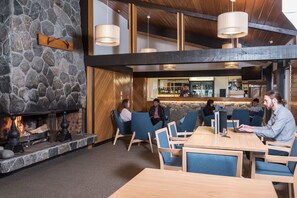 A modern interior with a stone fireplace, wooden ceiling beams, and a bar area. - Heartland Hotel Glacier Country (Fox Glacier)