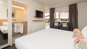 A hotel room with a large bed, a TV mounted on the wall, a bathroom with a sink and towel, and a view of the outside. - Heartland Hotel Glacier Country (Fox Glacier)