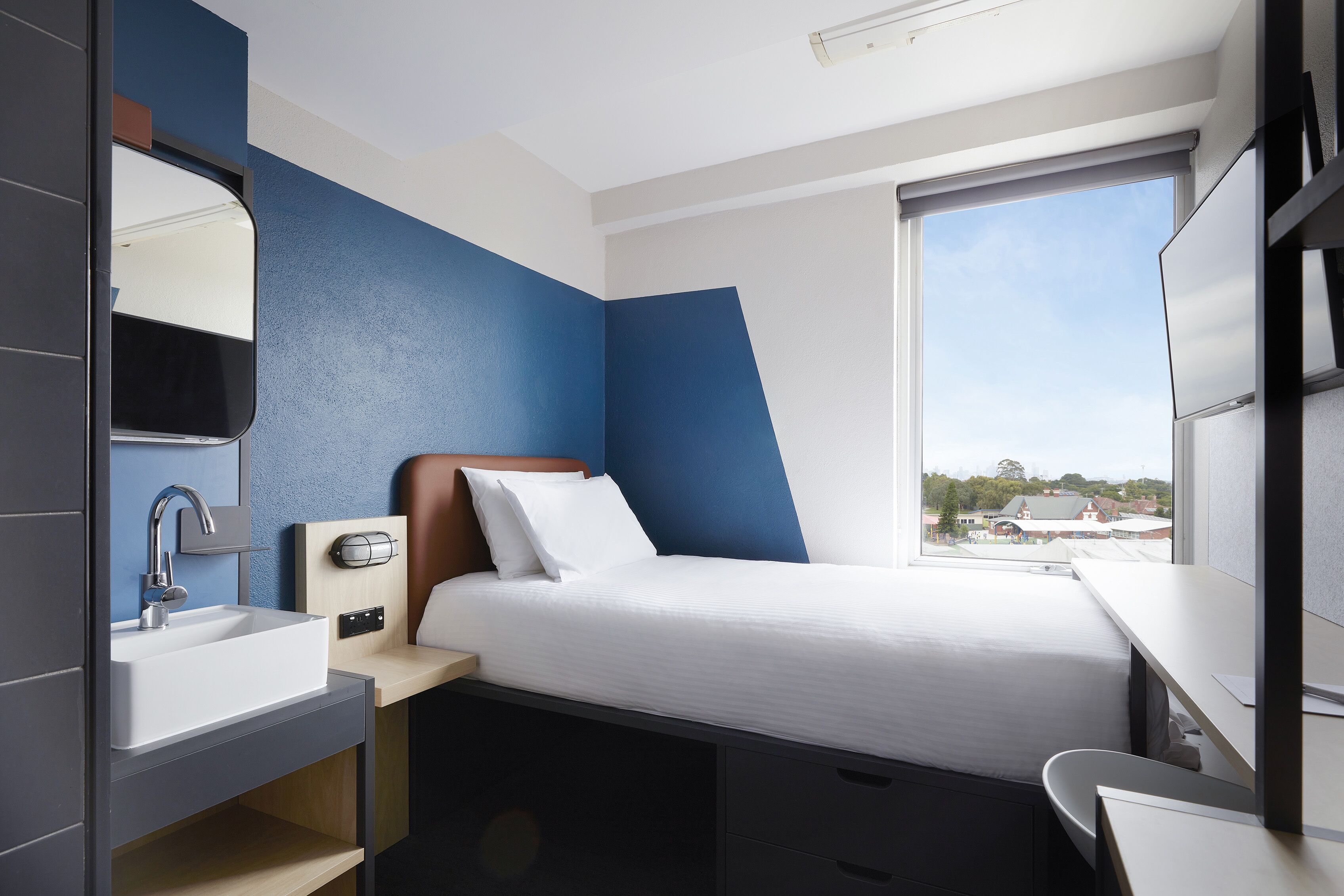 Una camera d'albergo moderna con un letto, un bagno con un lavandino e una finestra vista città.