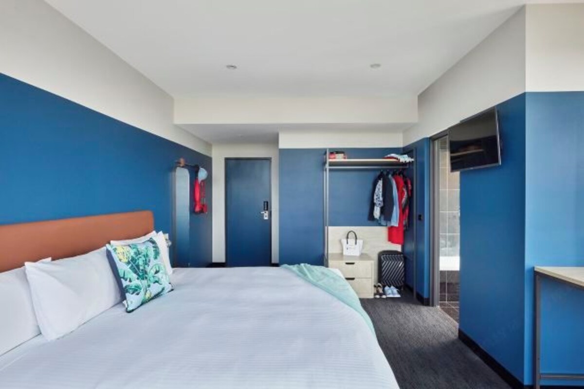A hotel room with a bed, a wardrobe, a desk, and a mirror.