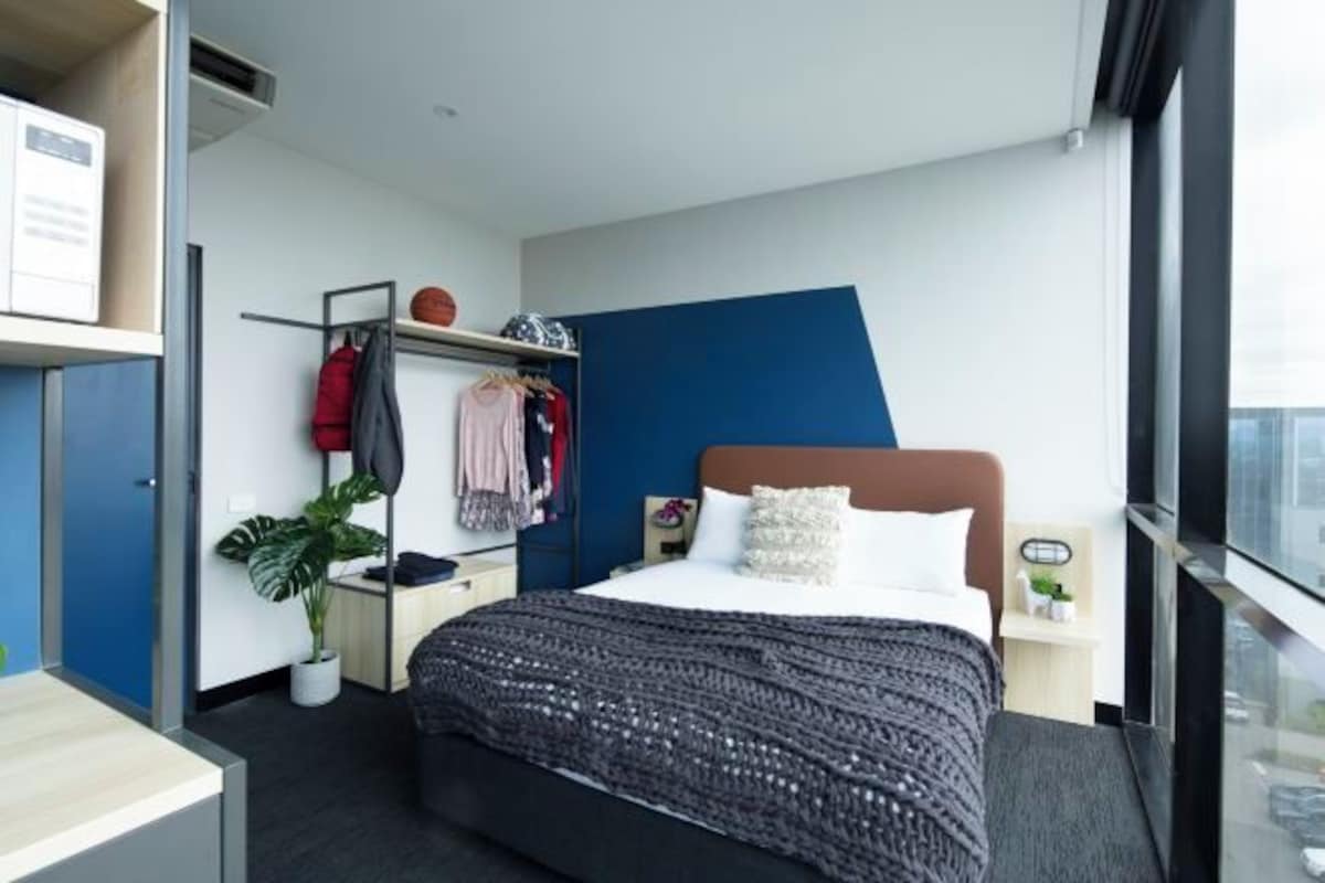 A modern hotel room with a large bed, a desk, a wardrobe, and a potted plant.