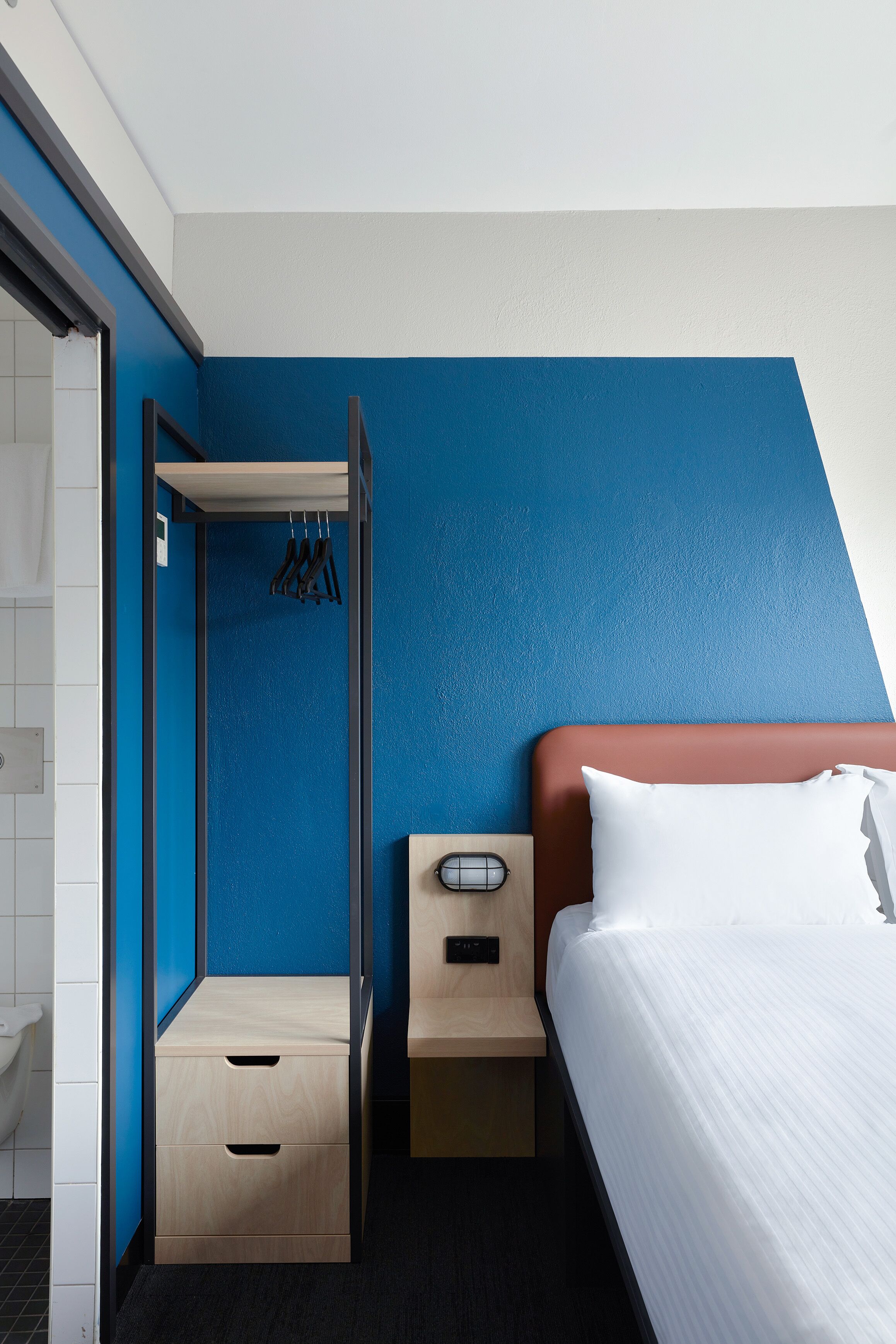 Habitación de hotel con cama, armario de madera, una mesita y un perchero.