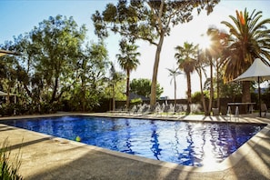 A swimming pool with lounge chairs and umbrellas, surrounded by trees and a clear sky. - Together Co-Living (Preston)