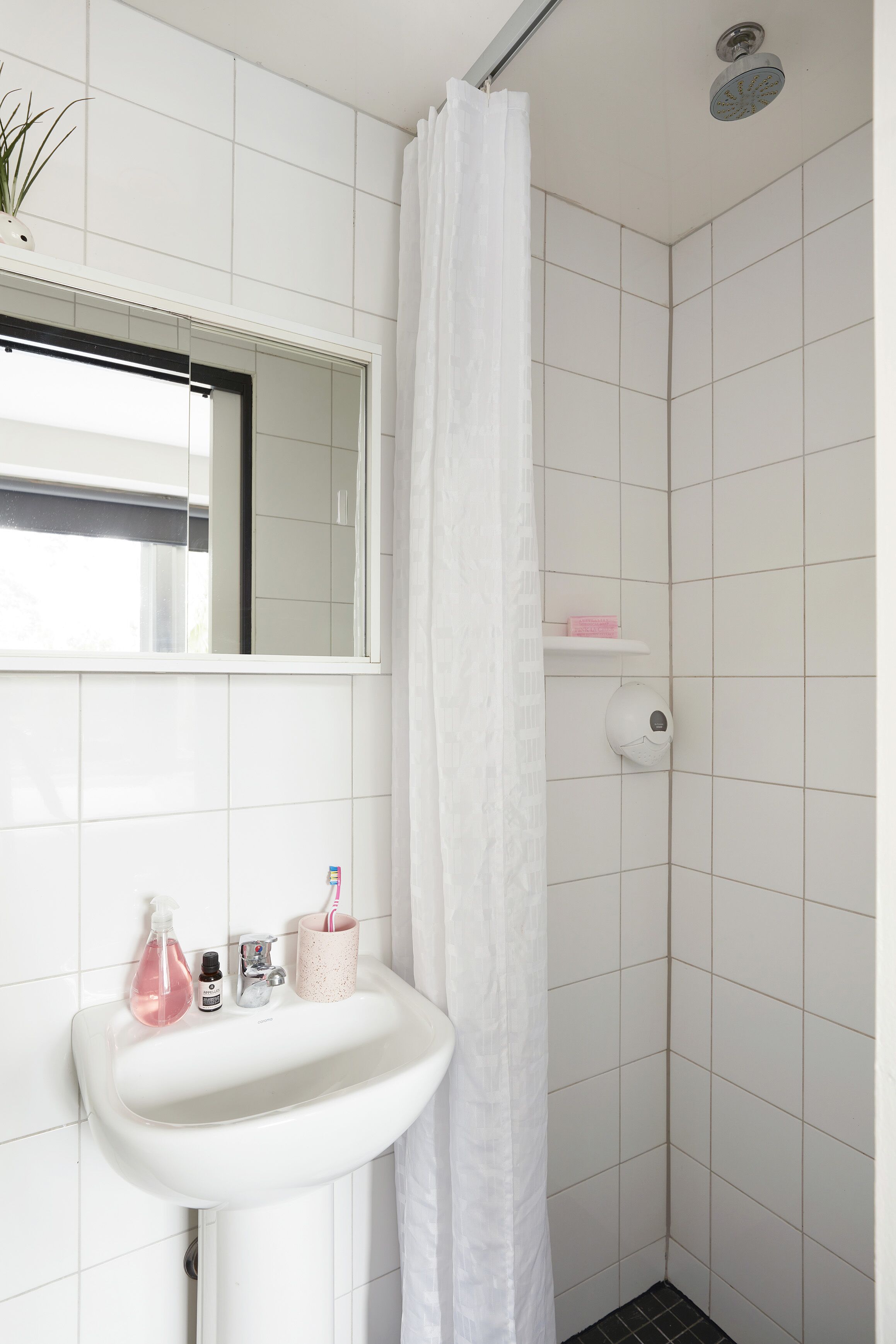 A bathroom with a white sink, a mirror, a shower curtain, and a shelf with toiletries.