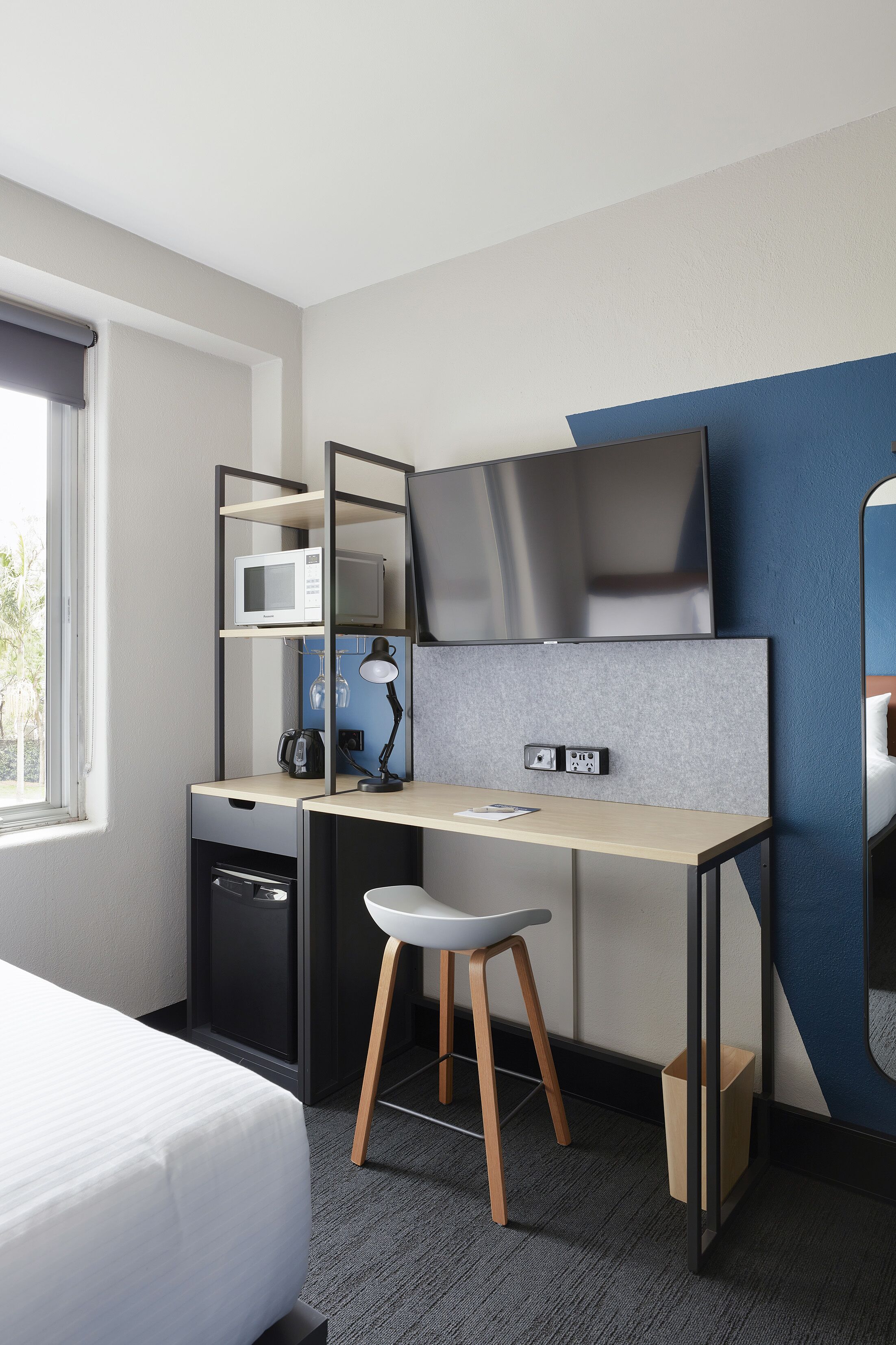 Une chambre d’hôtel moderne équipée d’un lit, d’un bureau avec un ordinateur, d’un four à micro-ondes et d’une télévision.