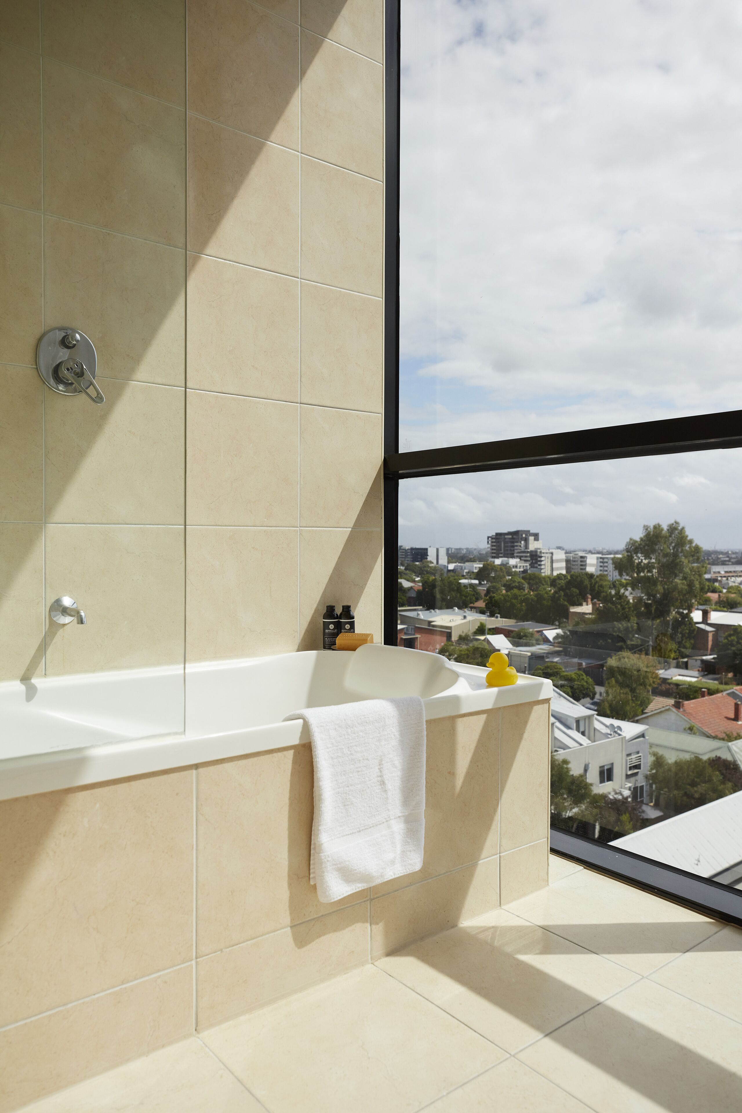 A modern bathroom with a bathtub, a large window, and a city view.
