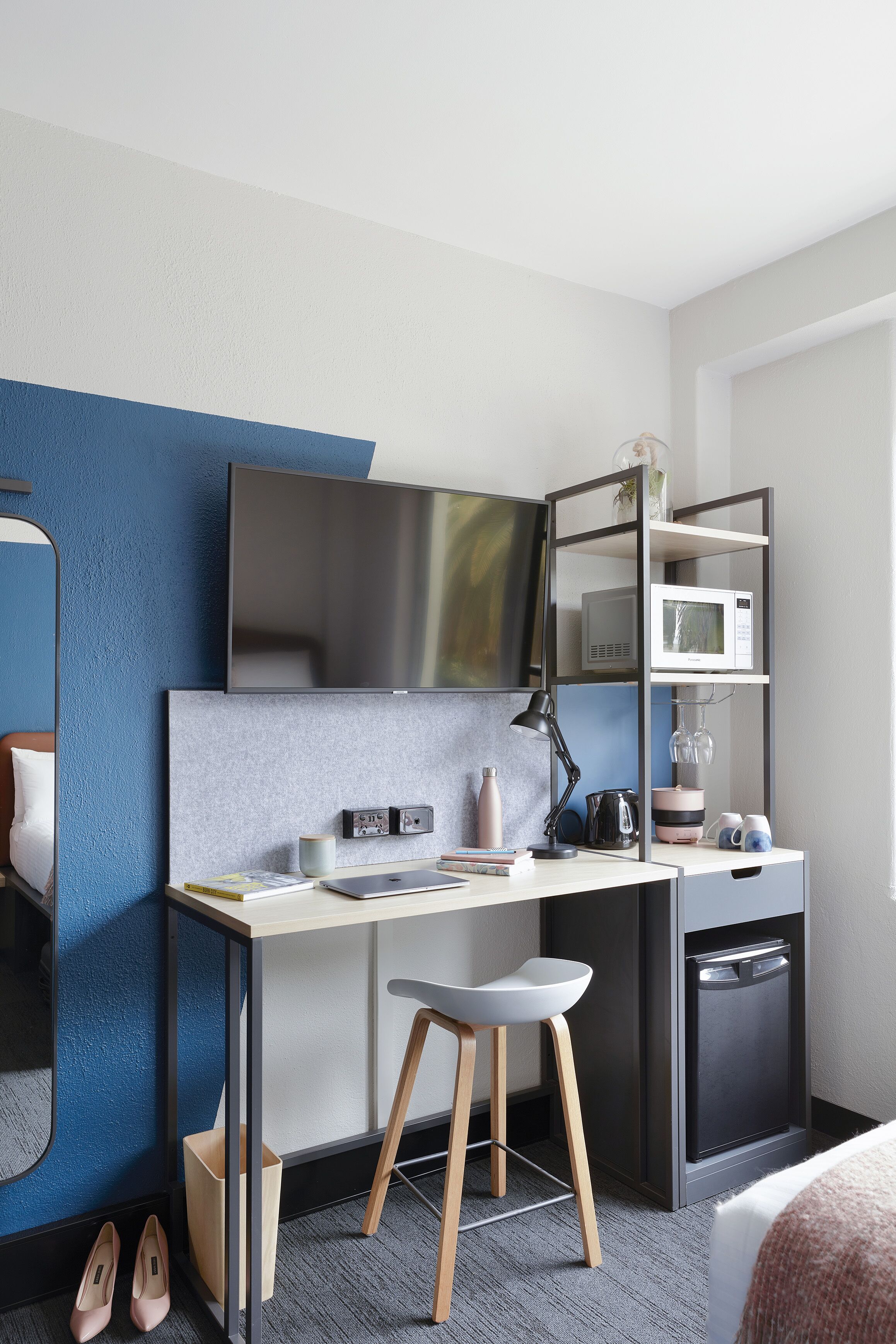 A modern hotel room with a desk, chair, TV, microwave, and a small refrigerator.