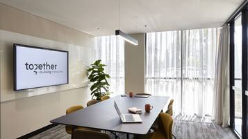 A conference room with a large screen displaying "Together co-living Melbourne", a laptop, a notebook, and a mug on the table.