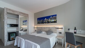 Une chambre d’hôtel avec deux lits, un minibar, un bureau avec une chaise et un tableau au mur.