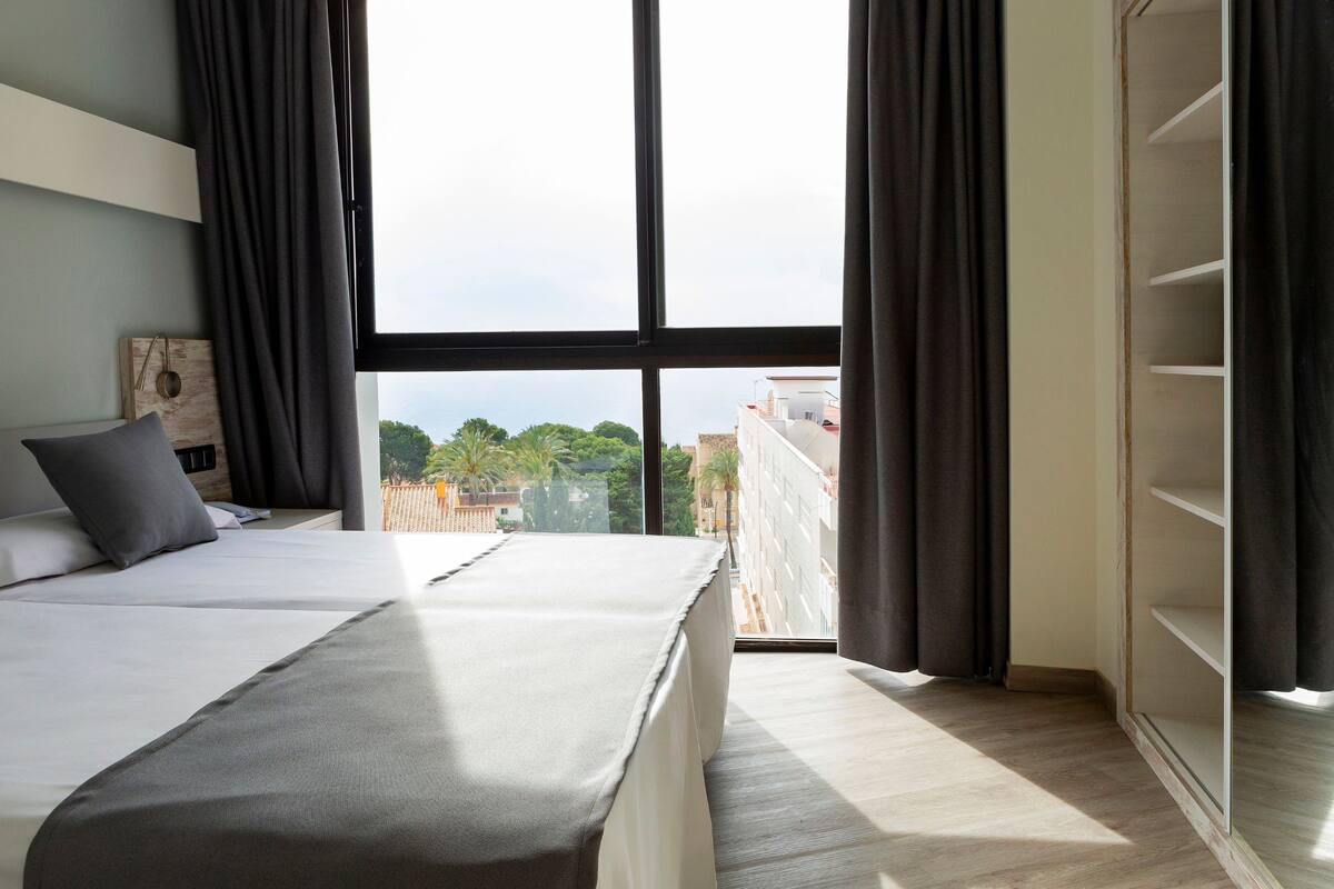 Een slaapkamer met een groot bed, een houten hoofdeinde, uitzicht op de stad door een groot raam en een inbouwkast.
