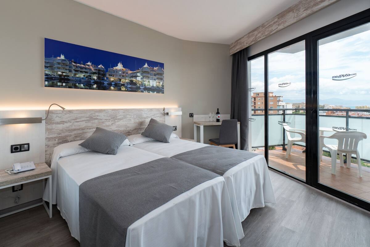 Een moderne hotelkamer met een groot bed, nachtkastjes, een bureau en een balkon met stoelen.