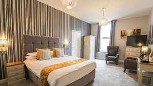 Quarto de hotel com uma cama grande, uma escrivaninha, uma cadeira, um guarda-roupa e uma televisão.
