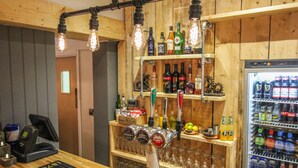 Uma área de bar com estação de chopp, prateleiras com garrafas de bebidas diversas e uma geladeira repleta de bebidas.