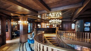 A grand wooden interior with a spiral staircase, chandeliers, and a view of the surrounding area. - Cristal Palace (Pinzolo)