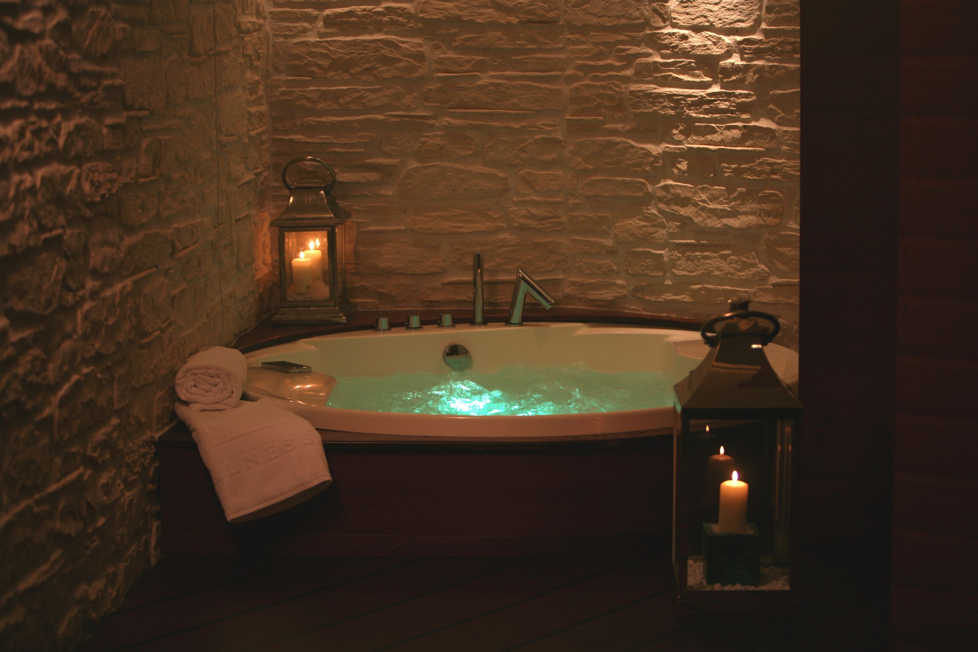 A stone-walled bathroom with a bathtub, two lit candles, and a towel.
