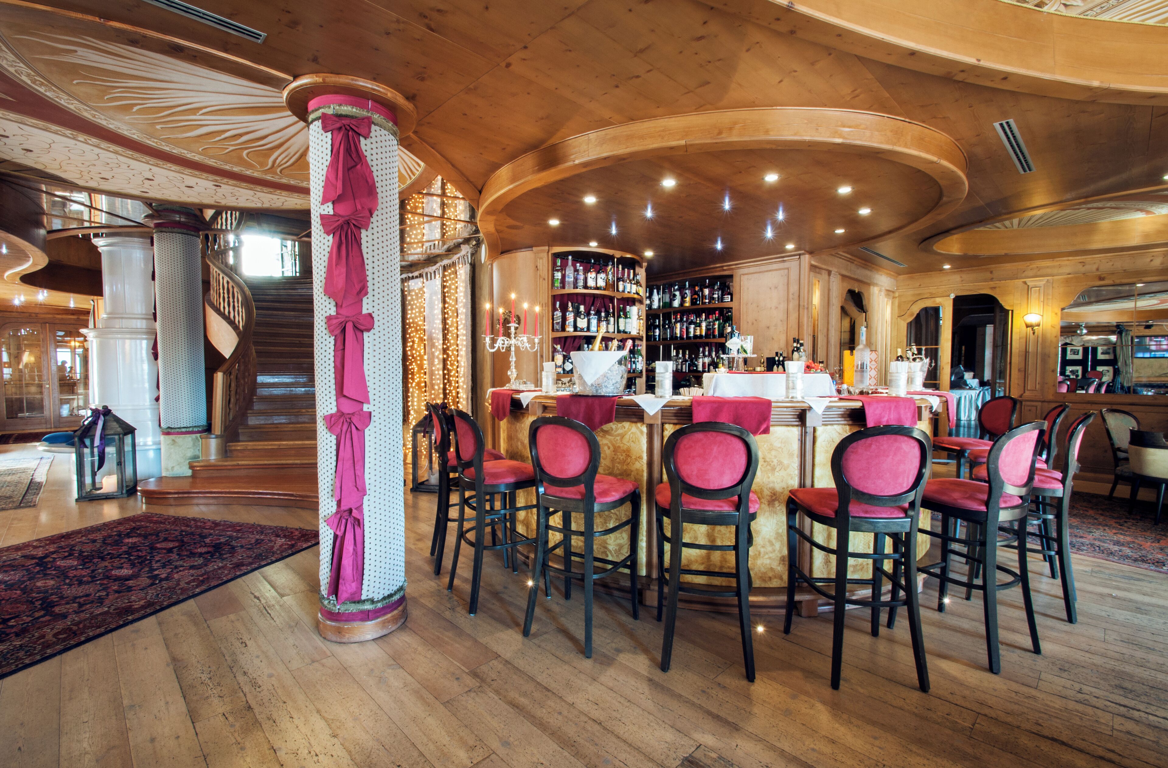 A bar area with wooden flooring, a central bar counter, and multiple bar stools.