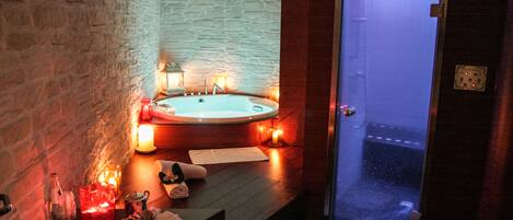 A spa room with a stone wall, a hot tub, candles, and a glass door leading outside.