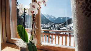 A window with a view of snow-covered mountains and a town below. - Cristal Palace (Pinzolo)