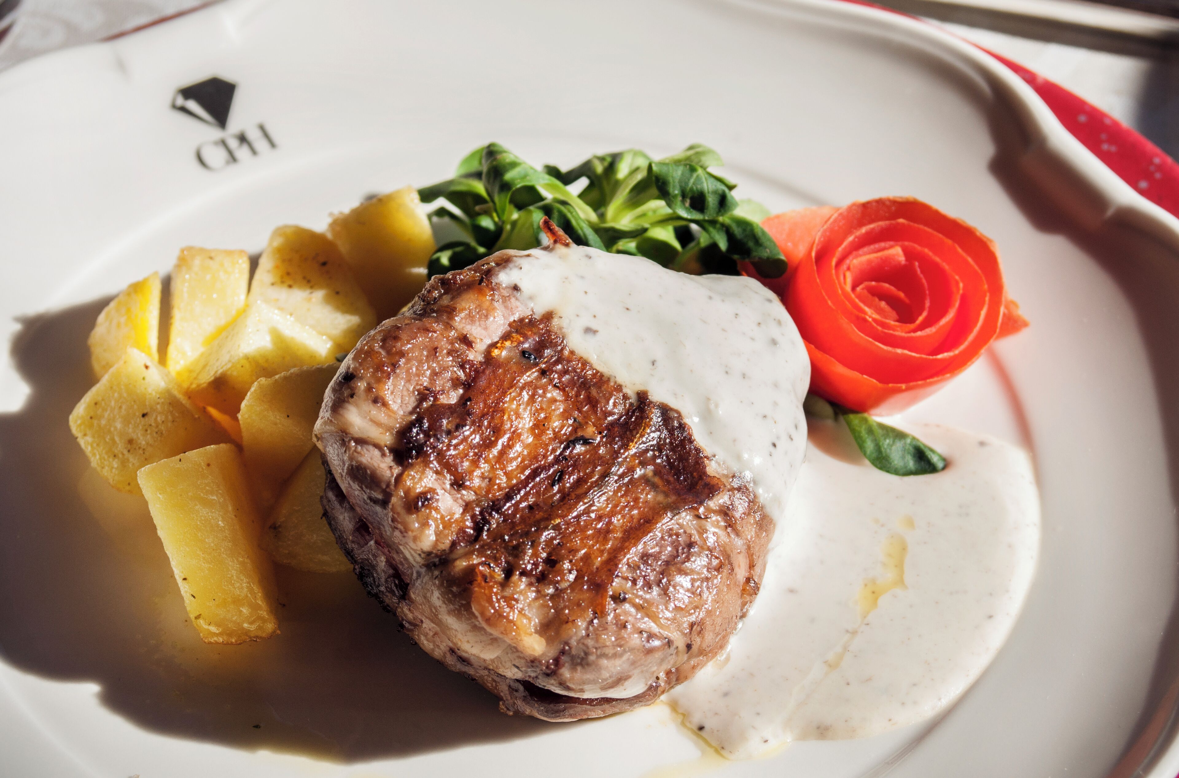 A plate with a grilled meat, potatoes, and a red vegetable garnish.