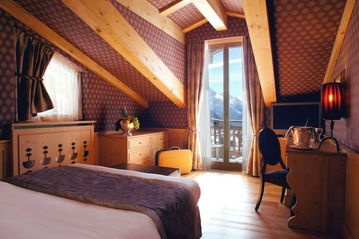 Una camera da letto mansardata accogliente con letto, comò e scrivania, caratterizzata da un'ampia finestra con vista sulle montagne.