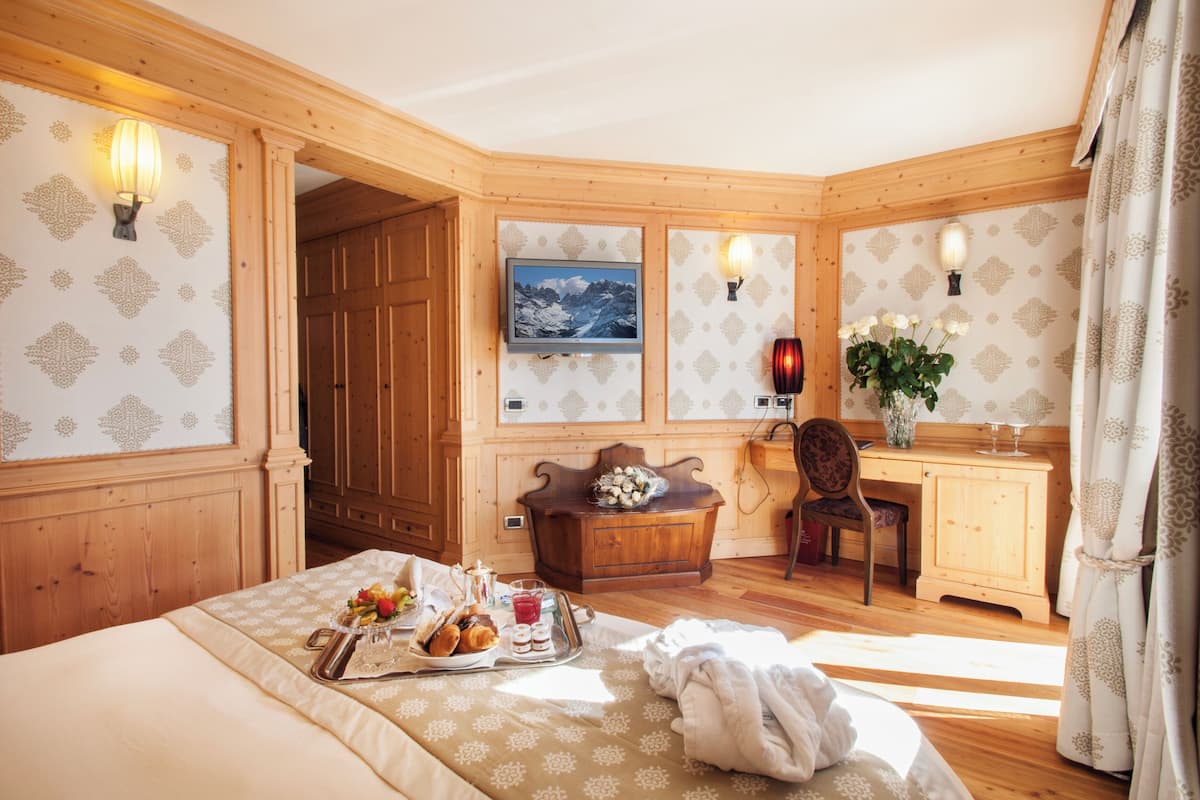Una camera accogliente con pannelli di legno, un letto con un vassoio per la colazione, una scrivania con una sedia e una TV a parete.