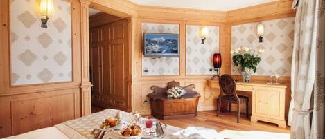 A cozy room with wooden paneling, a bed with a tray of breakfast, a desk with a chair, and a TV on the wall.
