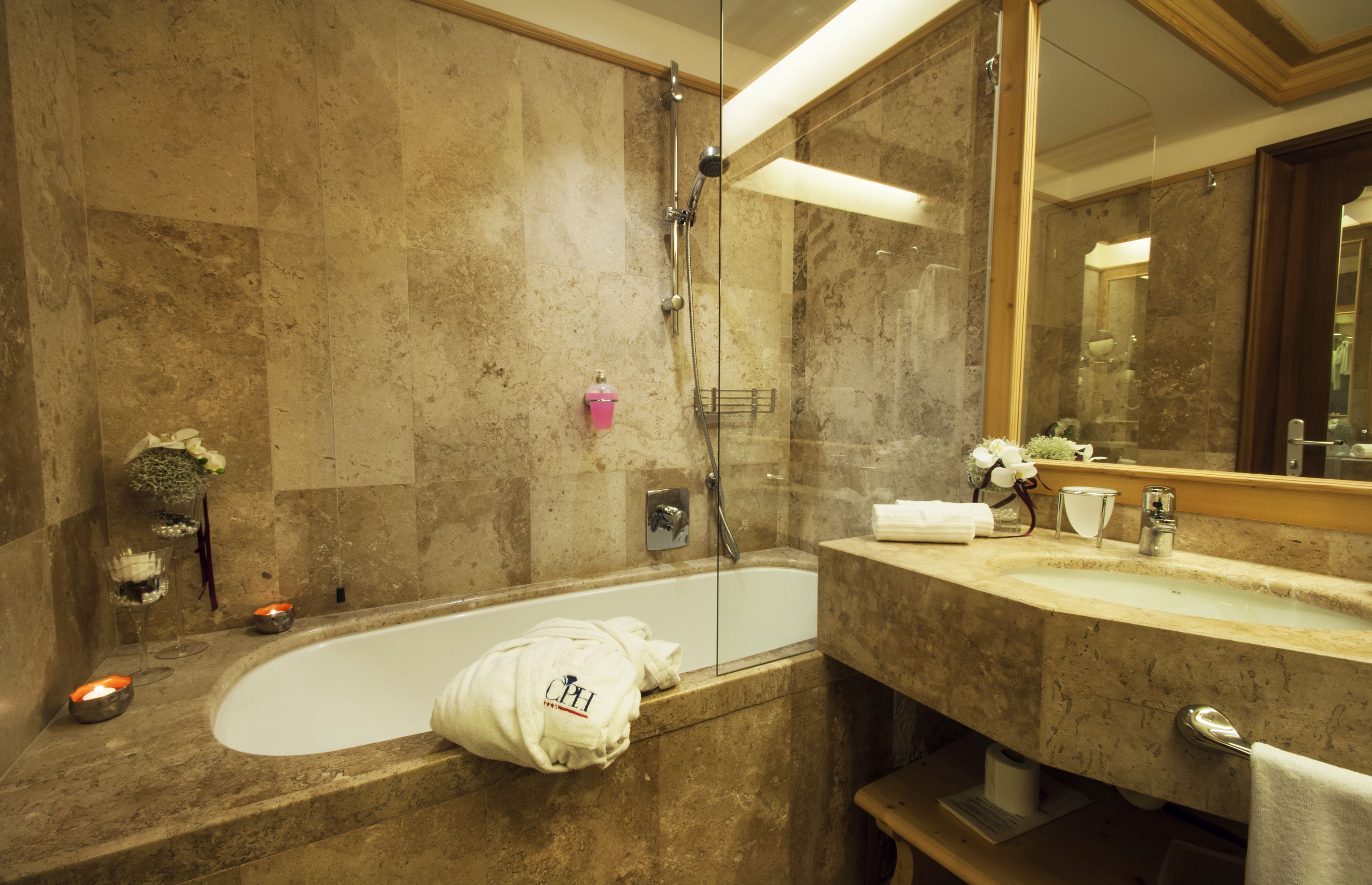 Une salle de bain avec une baignoire, une douche à parois de verre, un mur recouvert de carreaux de marbre, un lavabo avec un miroir et un porte-serviettes.