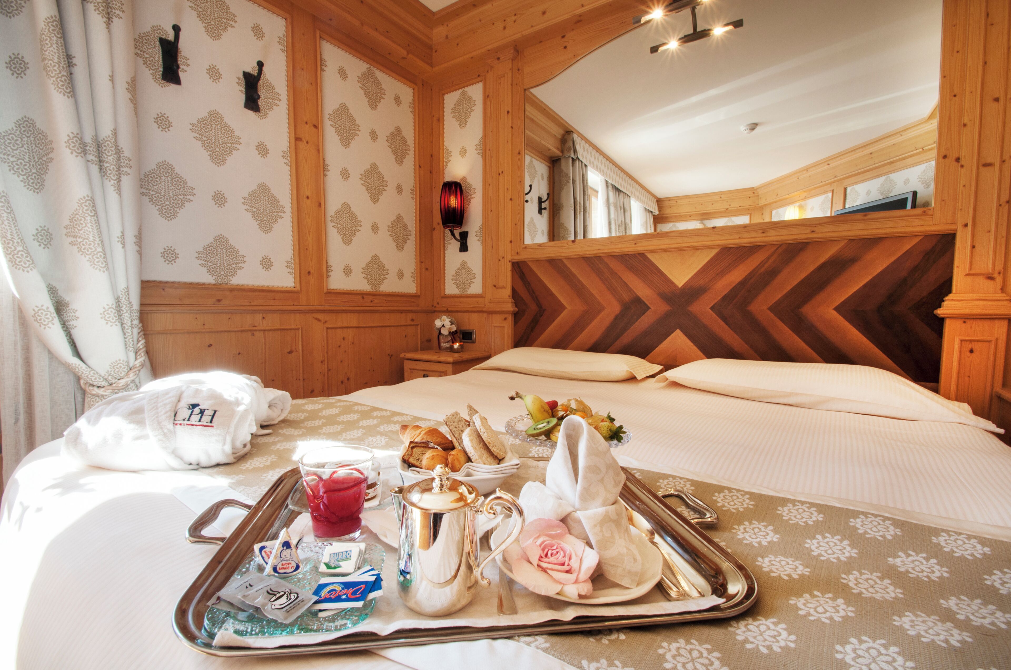 A hotel room with a bed, a tray with breakfast items, and a mirror reflecting the room's decor.