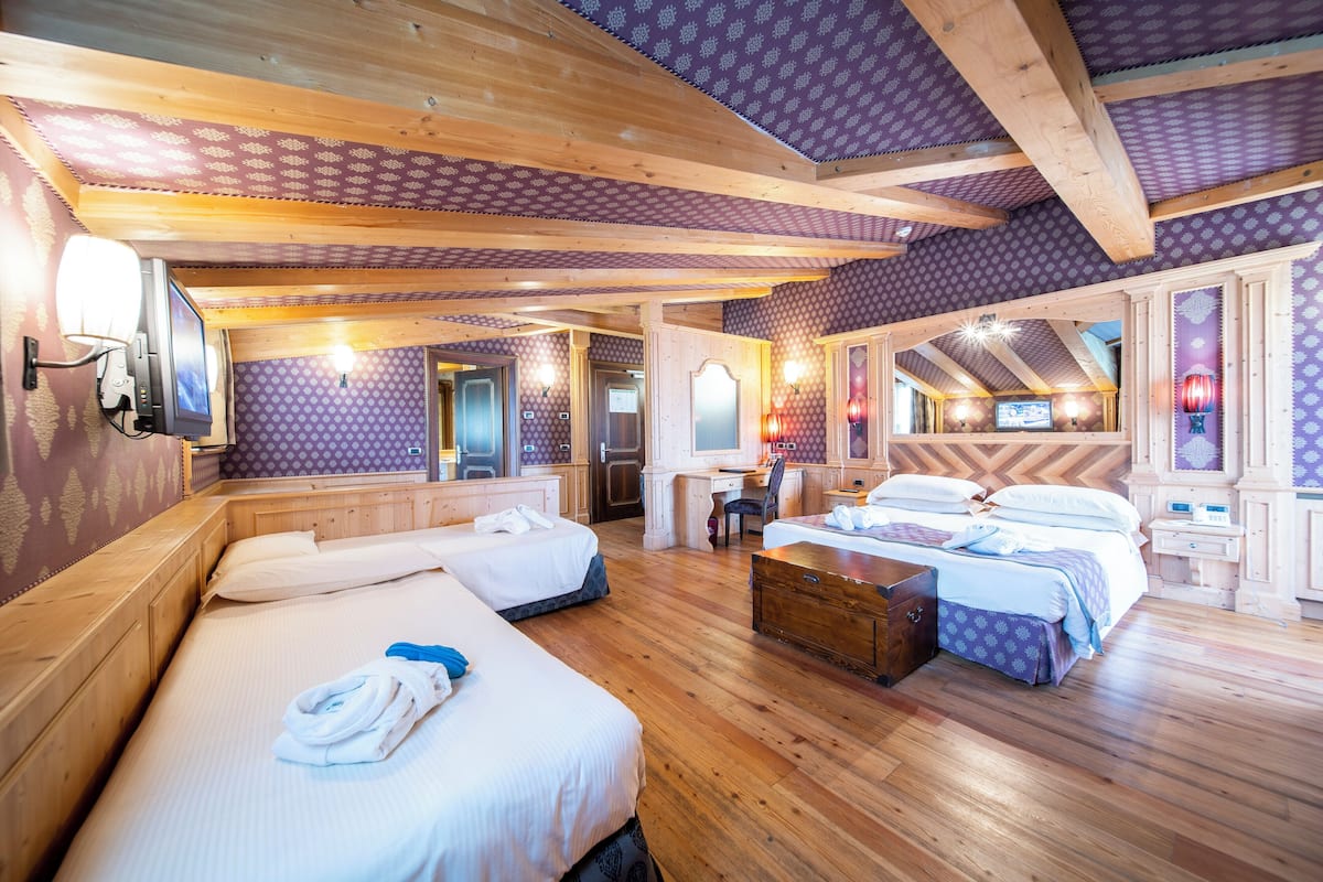 Una camera d'albergo con pavimento in legno, due letti, una scrivania e una televisione.