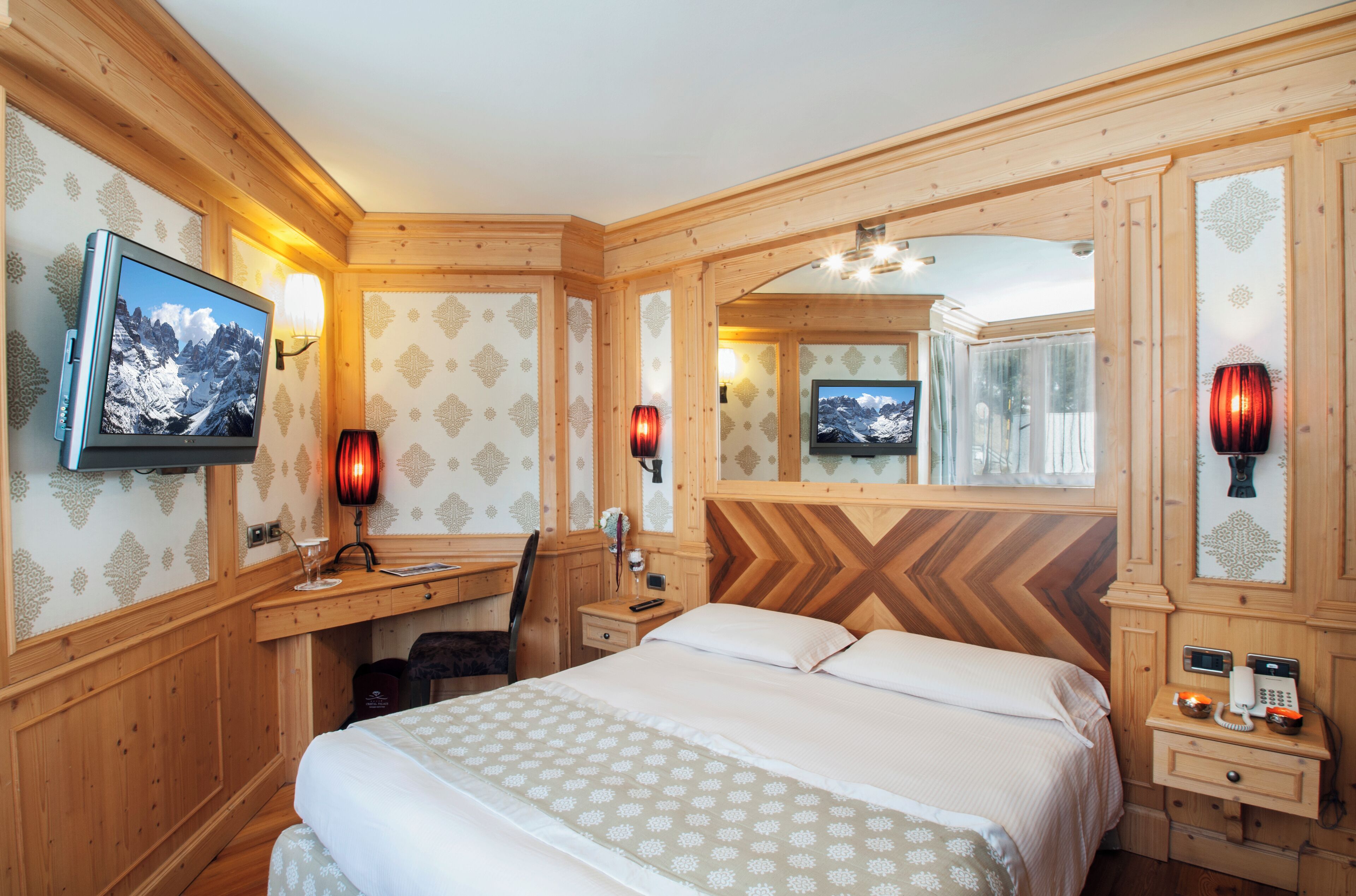 A wooden-paneled room with a bed, desk, and two wall-mounted televisions.