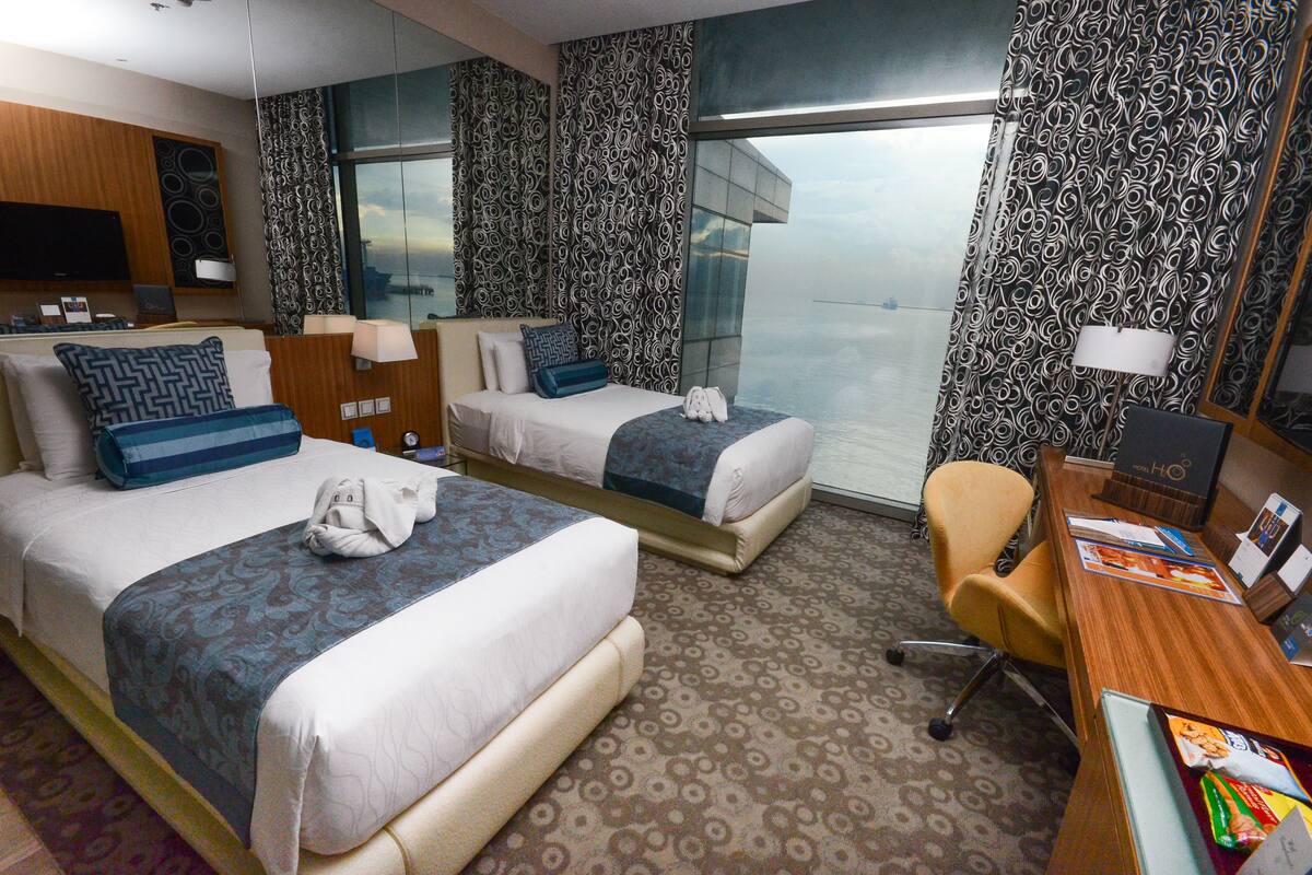 Ett hotellrum med två sängar, ett skrivbord, en stol, en TV och ett stort fönster med utsikt.