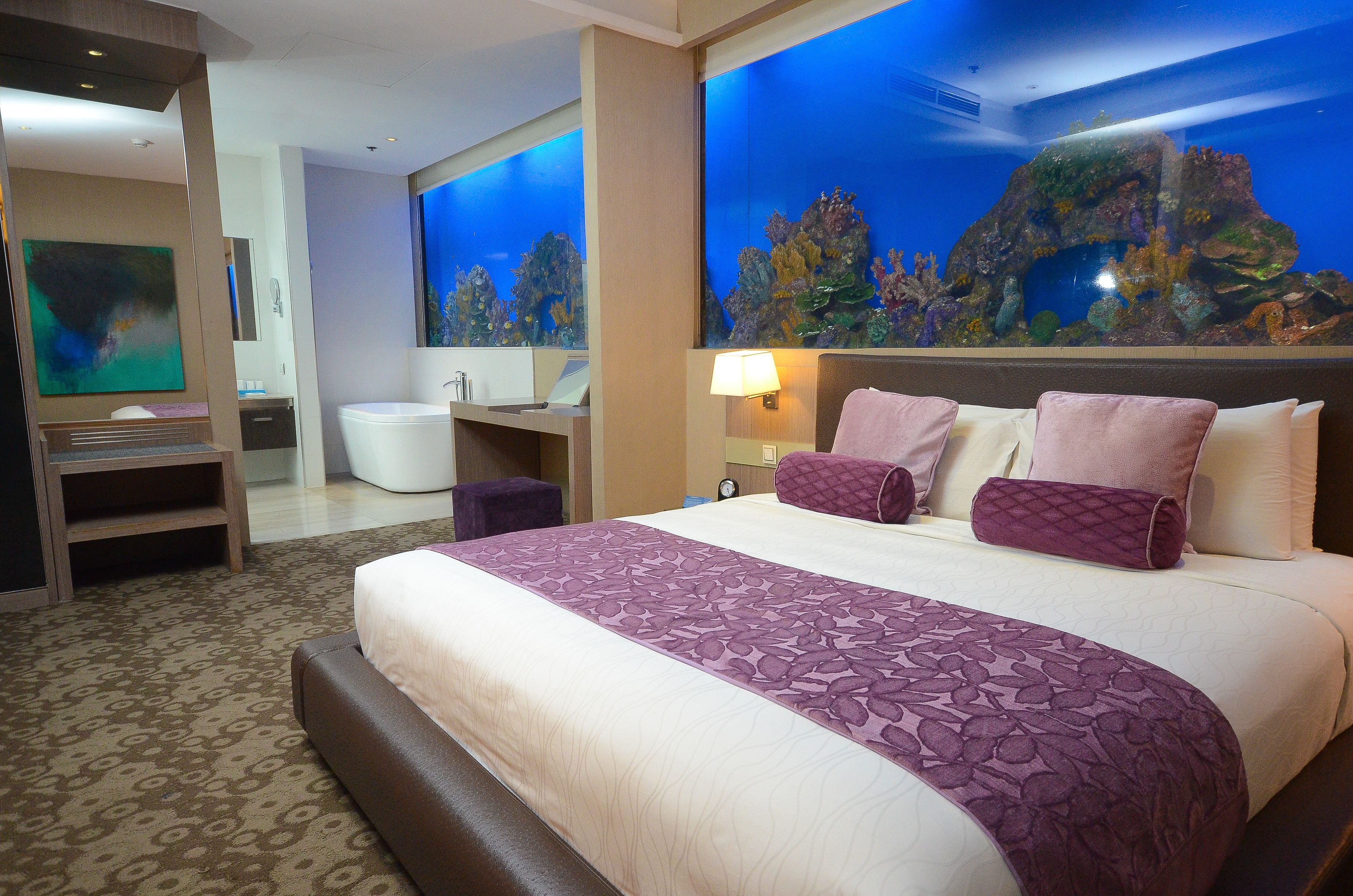 A hotel room with a large bed, a bathroom, and a wall mural of an underwater scene.