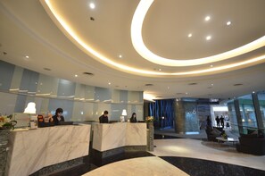 A modern hotel lobby with marble reception desks, a central seating area, and a curved ceiling design.