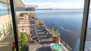 A terrace with outdoor seating overlooking a body of water, featuring a modern building in the background. - Hotel H2O (Manila)