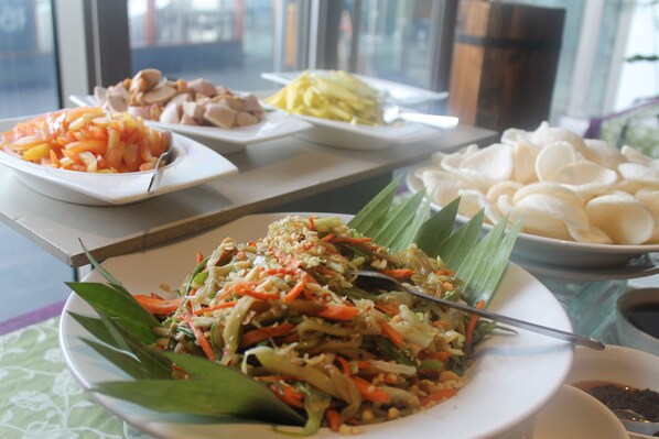 A table with various dishes including a plate of mixed vegetables, a plate of sliced meat, a plate of noodles, and a bowl of white rice cakes.
