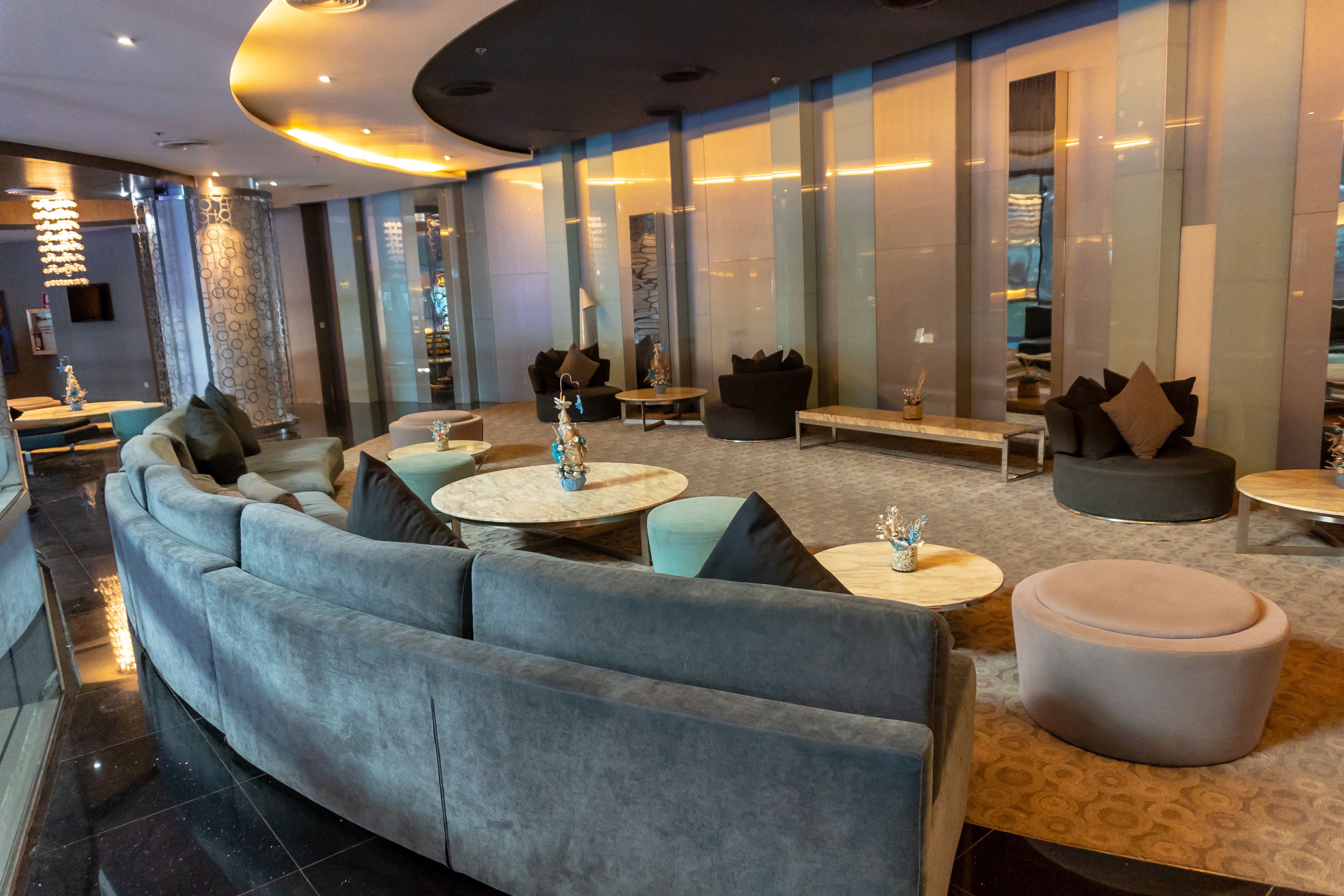 A modern lounge area with a large grey sofa, round tables, and a patterned ottoman.