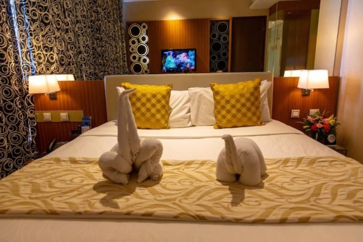 Una habitación de hotel con cama, almohadas, un televisor y apliques de pared.