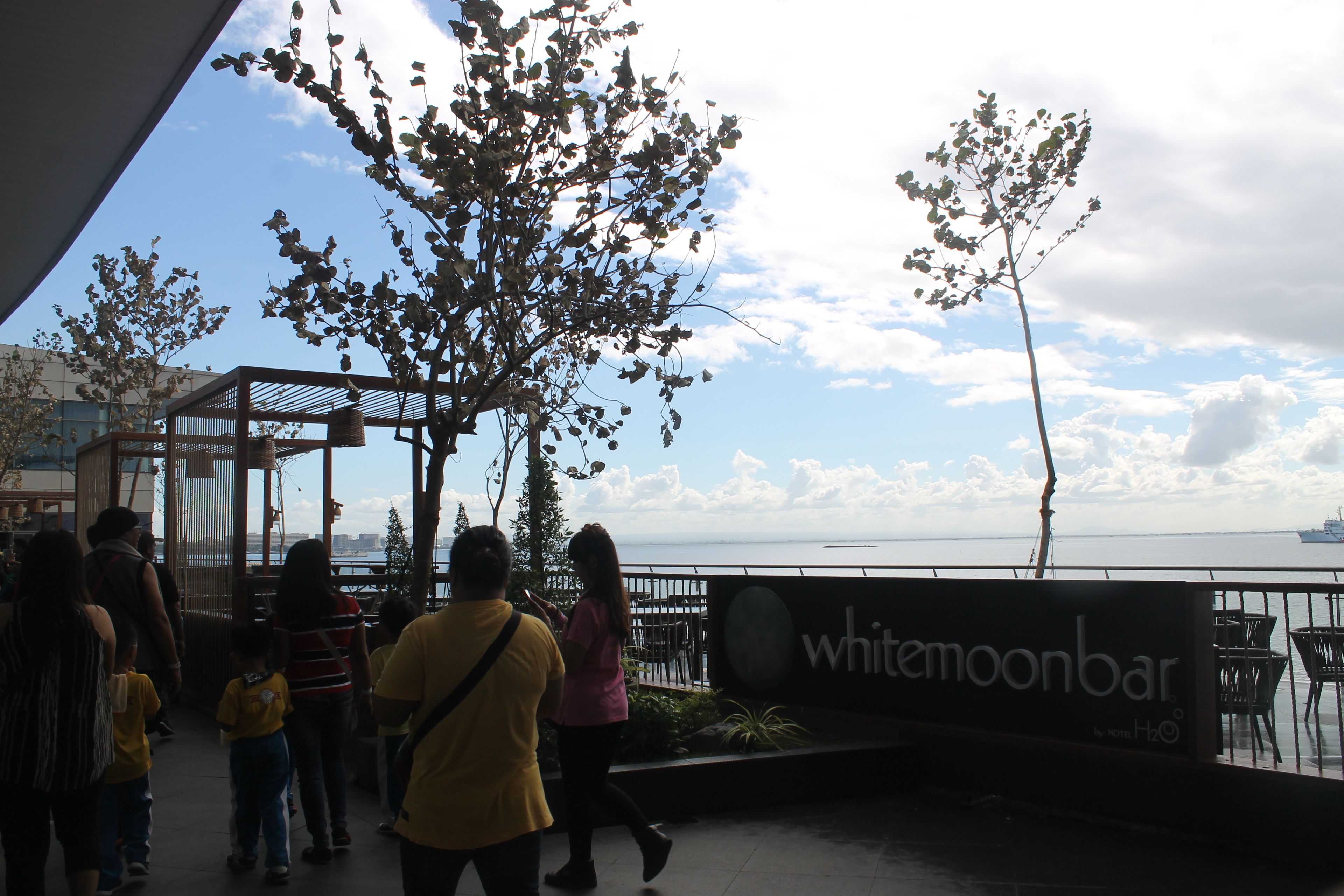 Un bar junto al agua llamado 'whitemoonbar' con vista al mar y un barco en la distancia.