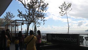 Un bar junto al agua llamado 'whitemoonbar' con vista al mar y un barco en la distancia.