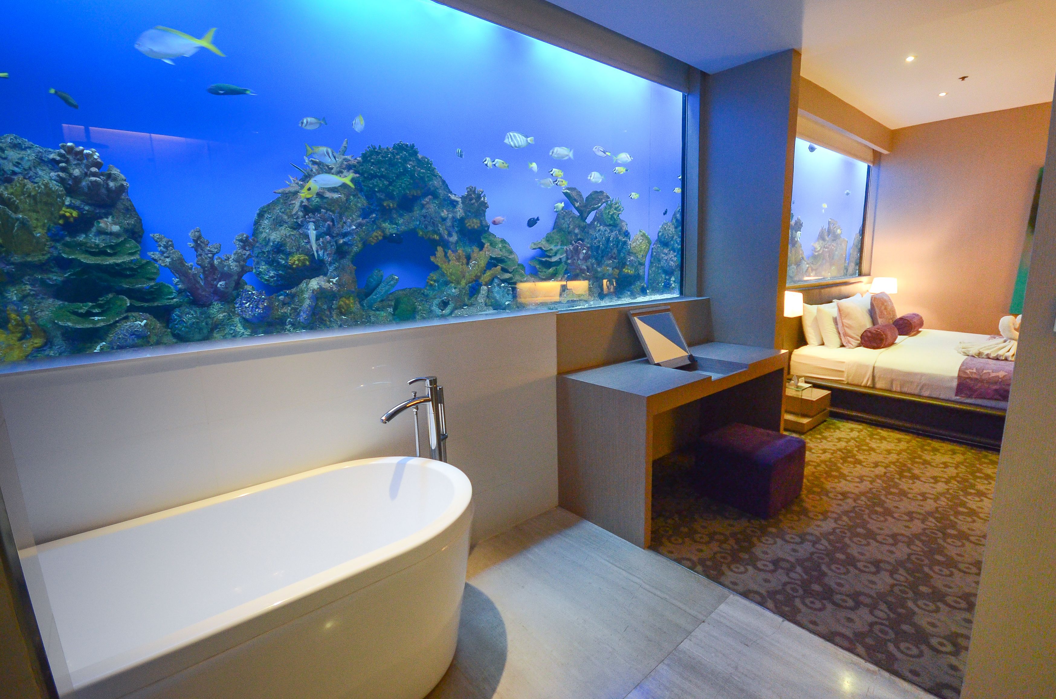 Un baño moderno con un acuario grande, una bañera independiente y una cama con una mesita de noche.