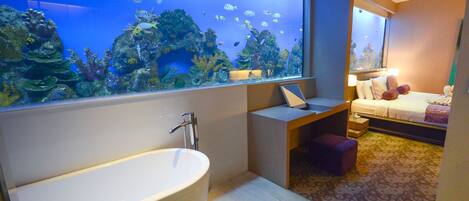 Un baño moderno con un acuario grande, una bañera independiente y una cama con una mesita de noche.