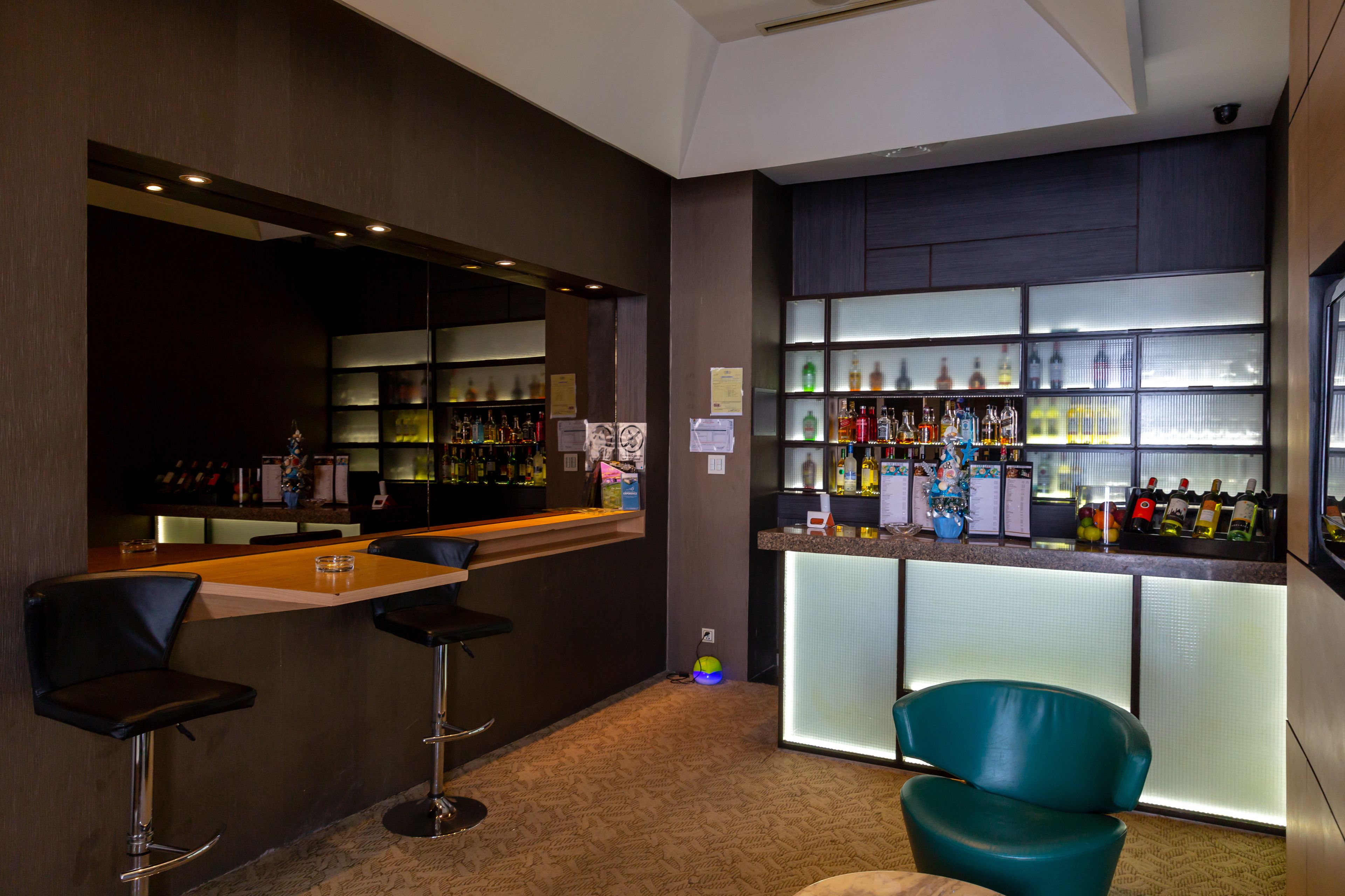 Una zona de bar con mostrador, taburetes y estantes llenos de botellas.