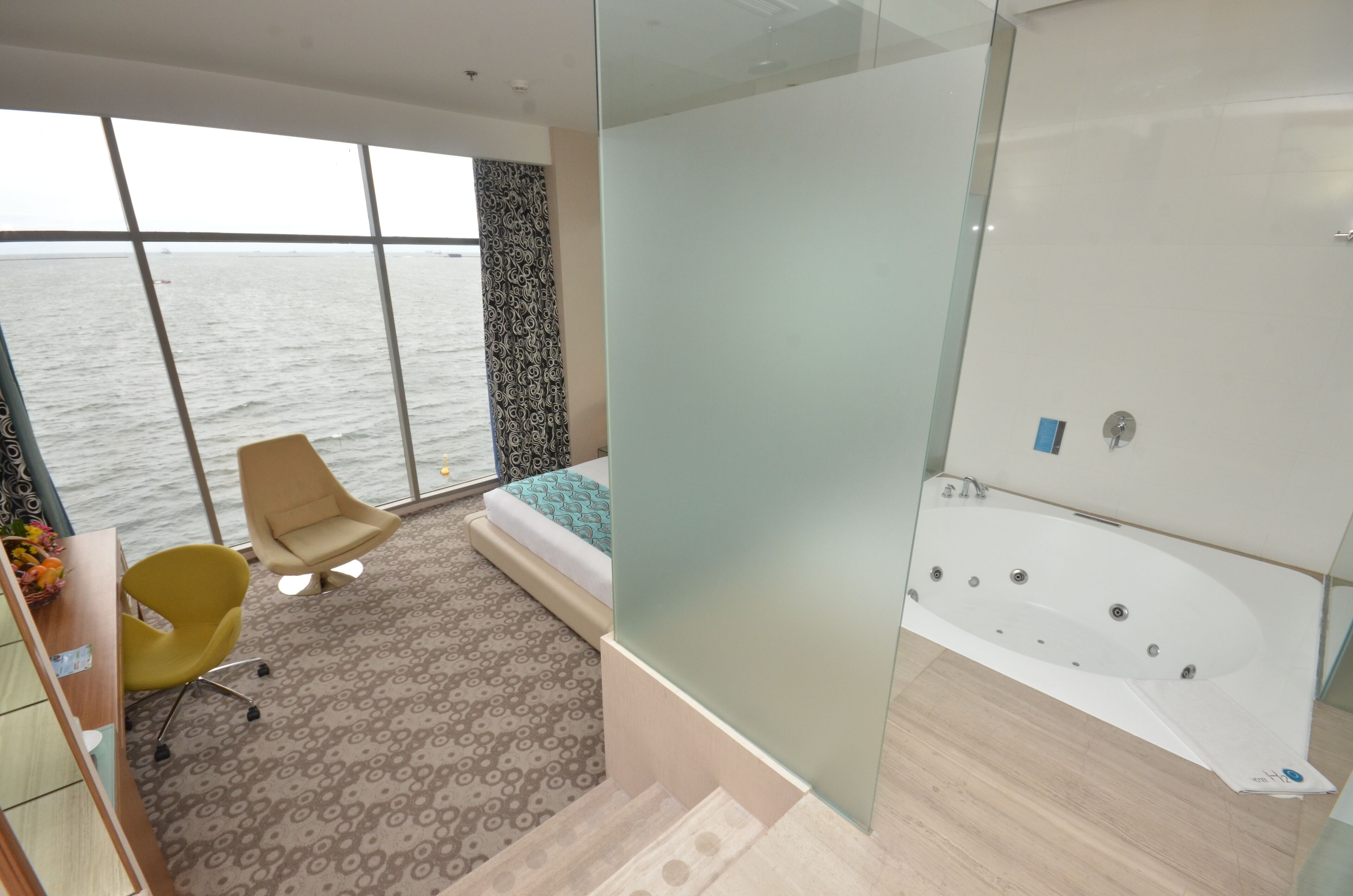 A modern room with a large window, a sofa, a desk, and a bathtub.