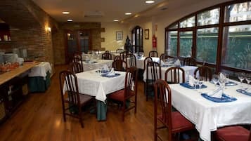 Un restaurante con varias mesas dispuestas para comer, suelo de madera y ventanas amplias que dejan entrar luz natural.
