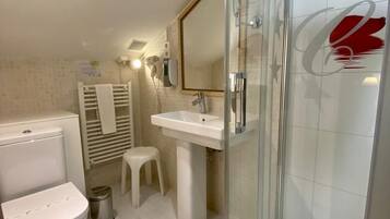 Un baño con inodoro, lavamanos y ducha con mampara de vidrio.